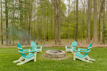 Stone Fire Pit with Teal Adirondack Chairs Circled Around in Wooden Area
