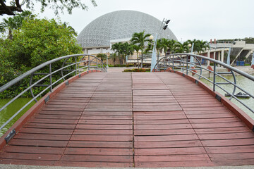 Low angle and diminishing perspective view of a wooden bridge in the park. The Centro Cívico building in the background, Guayaquil, Ecuador. Landscape photography.
