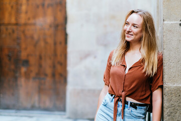blonde caucasian female tourist leaning on a wall of Barcelona old town. She is smiling and looking to one side