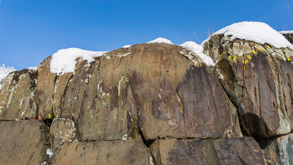 On the steep cliffs, ancient rock paintings are visible - drawings of people, animals. Lichen spots on the weathered surface. Snow on the stones. Blue sky. Altai. Kalbak Tash