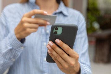 female hands hold a modern mobile phone and a bank credit or debit card on the street..ordering purchases, working online, transferring money by phone