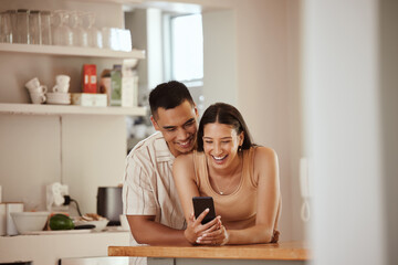 Happy couple browsing on a phone and laughing at funny social media videos on her phone while relaxing together at home. Carefree, smiling and young boyfriend hugging his girlfriend in the kitchen