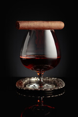 Snifter of brandy and cigar on a black background.