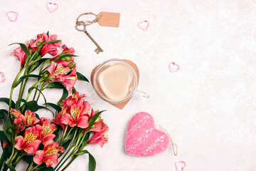 Bouquet of Alstroemeria flowers, cup of coffee, and key with tag on a white marble background.