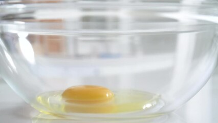 Crack an egg straight into a glass bowl at home kitchen to making cake.