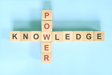 Knowledge is power concept. Wooden block crossword puzzle flat lay in blue background.
