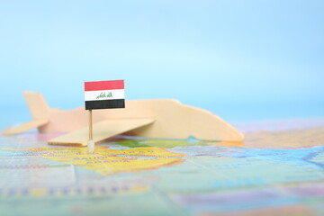 Selective focus of Iraqi flag in blurry world map and wooden airplane model. Iraq as travel and tourism destination concept.