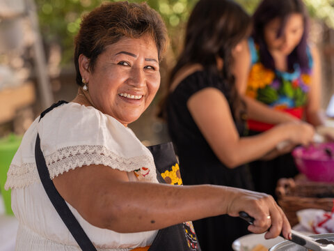 Older woman smiling and cooking Indigenous foods with her daughters 