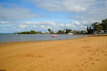 Obraz premium Sandy beach with boats, houses in the background and pretty cloudy sky. Victoria Point, Queensland, Australia 