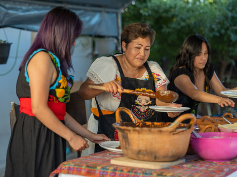 Wide angle view of an Indigenous mother pouring mole onto a dinner plate for her daughters