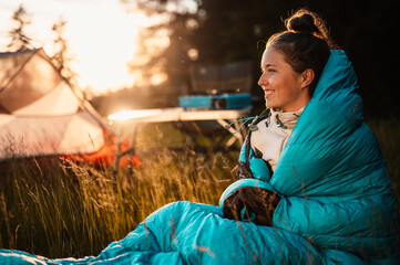 Woman relaxing and lie in a sleeping bag in the tent. Sunset camping in forest. Mountains landscape...
