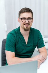 Handsome physician sitting in the office. Young clinical specialist working with computer.