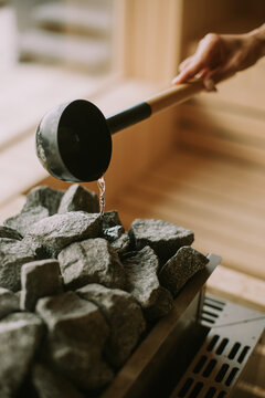 Hand of young woman pouring water on hot rocks in the sauna
