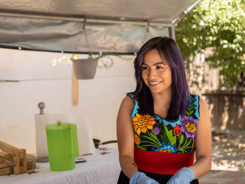 Horizontal image of an Indigenous woman smiling while working with chiles in an outdoor kitchen 