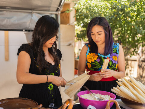 Horizontal image of twin sisters beginning to make tamales 