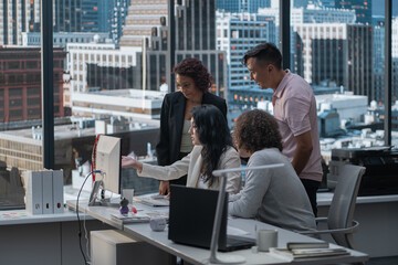 Diverse team of employees brainstorming, gathering around the computer screen. Discussing project, new ideas, company development