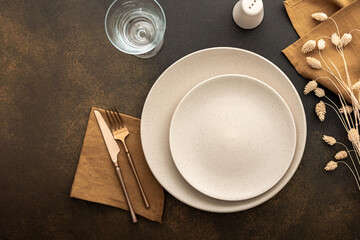 Table setting, empty plate with napkin and cutlery on a brown background, top view of the served table decorated with dry flowers - obrazy, fototapety, plakaty