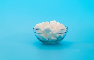 Sugar cubes in a bowl on blue background