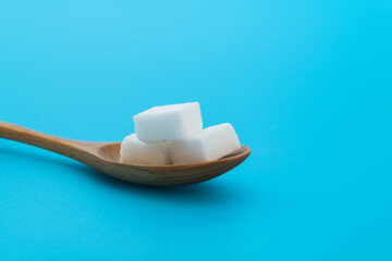Sugar cubes in wooden spoon on blue background