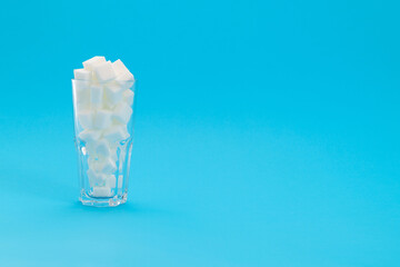 Glass cup full of sugar cubes on blue background