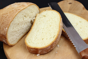 Wooden cutting board with sliced white bread and knife on black background.