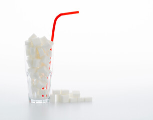 Glass cup full of sugar cubes on white background