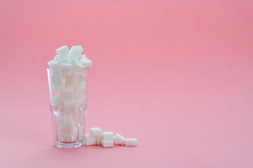 Glass cup full of sugar cubes on pink background