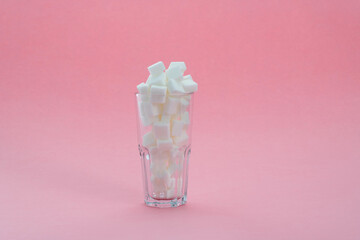 Glass cup full of sugar cubes on pink background