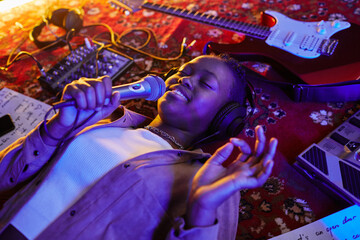 Closeup of smiling black woman holding microphone and singing lying on carpet in purple neon light