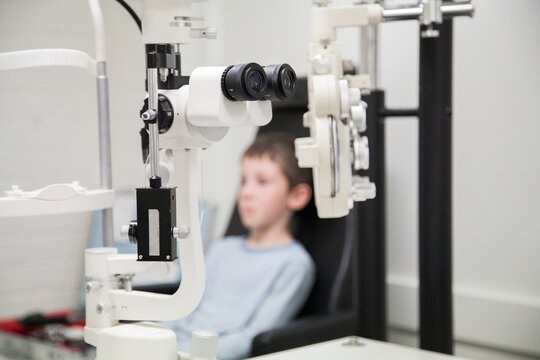 Eye testing machines and boy in chair in an optometrist's white room
