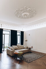 an example of a living room interior in a neo-classical style with modern elements. a sofa in the middle of a room with high ceilings and moldings.