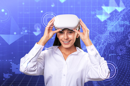 Happy young european businesswoman with VR glasses standing on creative glowing blue metaverse background. Cyberspace, augmented reality, future and technology concept.