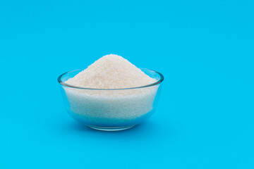 Granulated sugar in a bowl on blue background