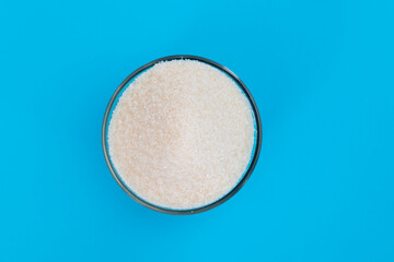 Granulated sugar in a bowl on blue background