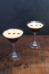 Glasses of espresso martini with coffee beans on wooden table and black background