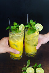 Hands clinking glasses with mango mojito on black background