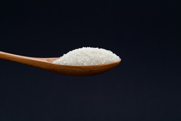 Wooden spoon with sugar crystals on black background