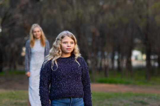 aboriginal girl with long blonde looking into distance with her mum blurred in the background
