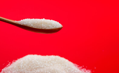 Wooden spoon with sugar crystals on red background