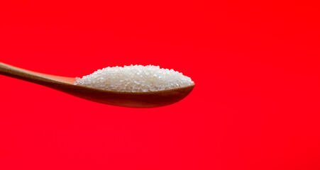 Wooden spoon with sugar crystals on red background