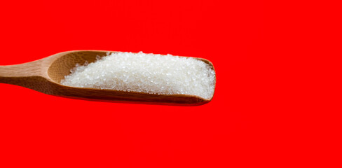 Wooden scoop with sugar crystals on red background