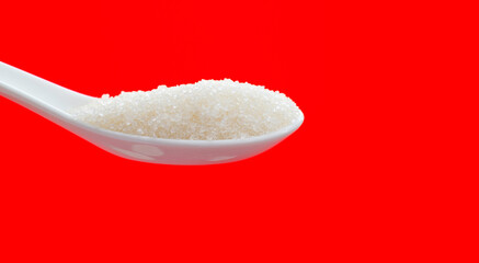 Ceramic spoon with sugar crystals on red background