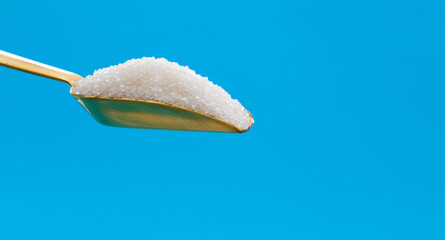 Steel scoop with sugar crystals on blue background