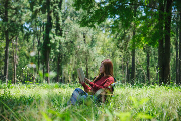 Portrait of a beautiful young asian woman reading a book while sitting on a camping chair in the park