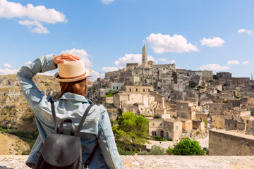 tourist girl with hat  looking the stunning view of the Sassi di Matera in Italy on a warm summer day. Travel destination, adventure, success and exploration concept. - obrazy, fototapety, plakaty