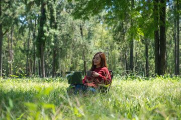 A beautiful asian woman drinking coffee and working on laptop keyboard while sitting on a chair in the park