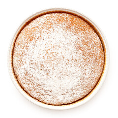 Whole lemon sponge cake with icing sugar topping in a paper tray isolated on white from above.