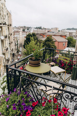 a coffee table and two chairs on an open balcony with a city view. blooming flowers in pots decorate the balcony	
