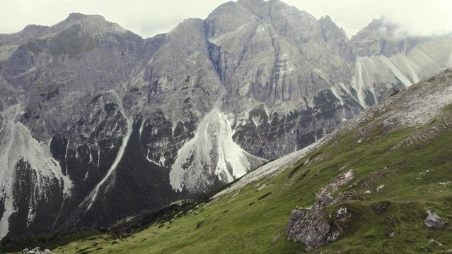 Beautiful aerial of alpine mountains (Stubai, Austria). Grass and a trail in the foreground. Tilting up with an Alpine mountain scenery and a valley in the distance on a clear sunny day. 4K