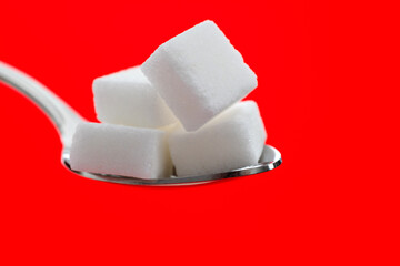 Sugar cubes in a spoon on red background